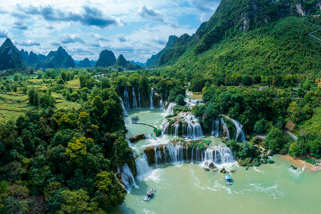 Panoramic view of Ban Gioc Waterfall cascading over limestone cliffs surrounded by lush greenery