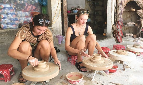 Foreigner sitting at a pottery wheel shaping clay in a traditional workshop at Bat Trang Ceramic Village