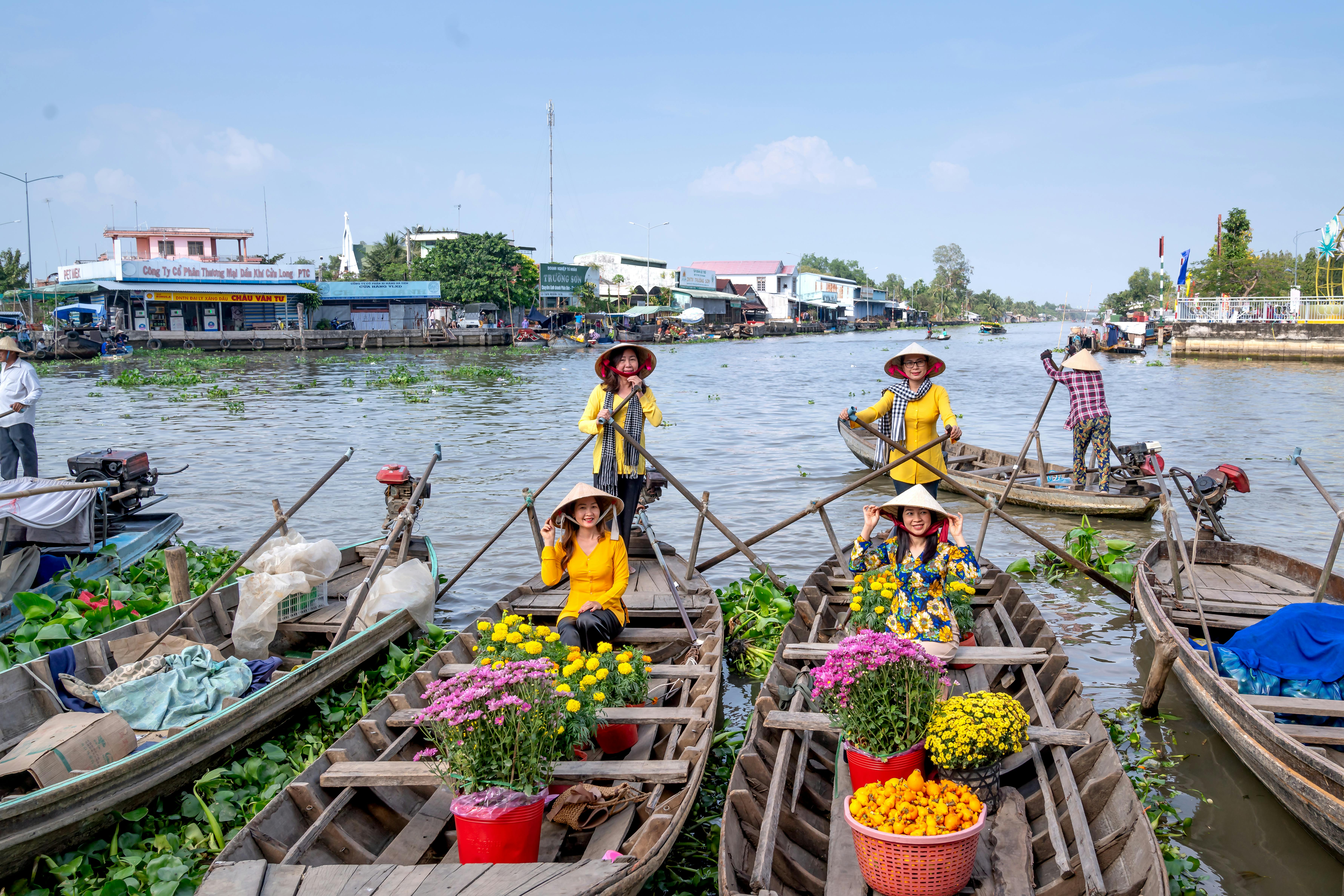 Women in traditional áo bà ba row flower-filled boats at a floating market